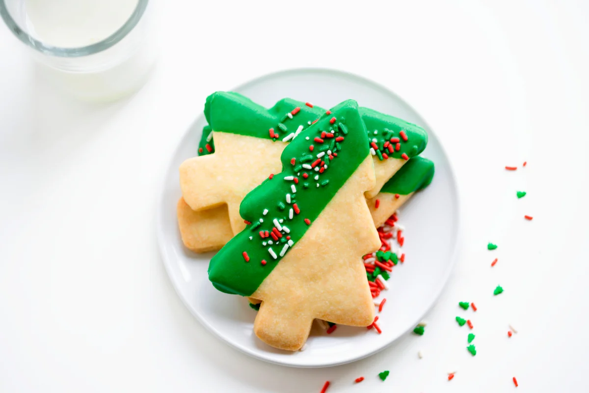 Shortbread Christmas tree cookies on white plate with glass of milk