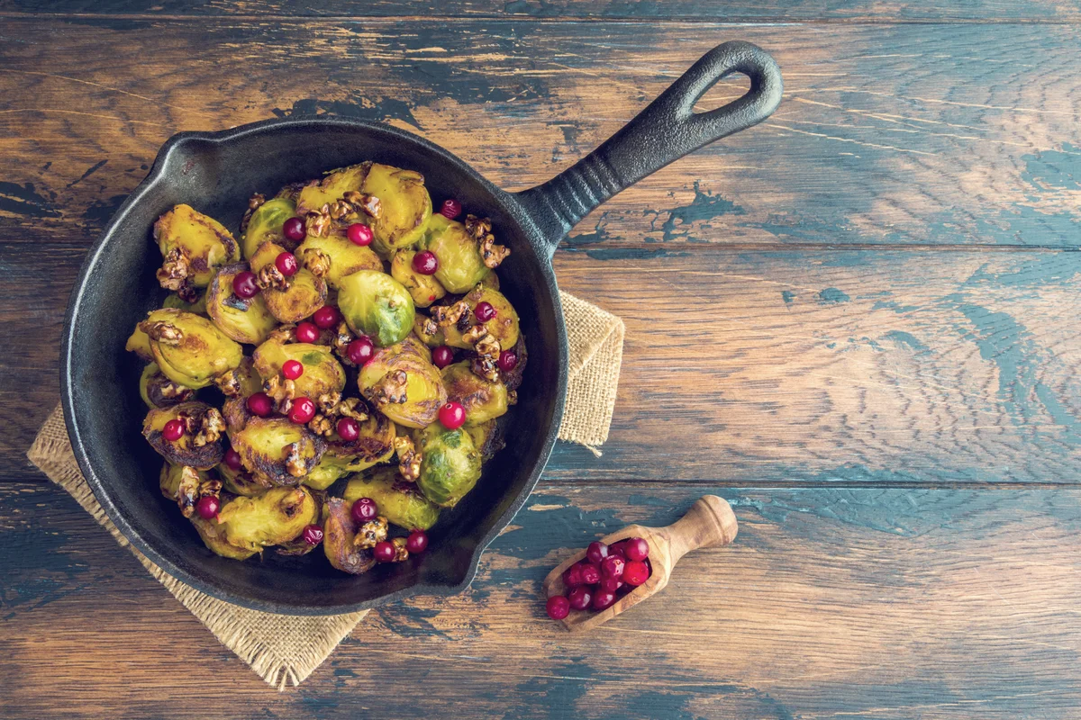 Roasted Brussels sprouts with caramelized walnuts and cranberries in a cast iron frying pan