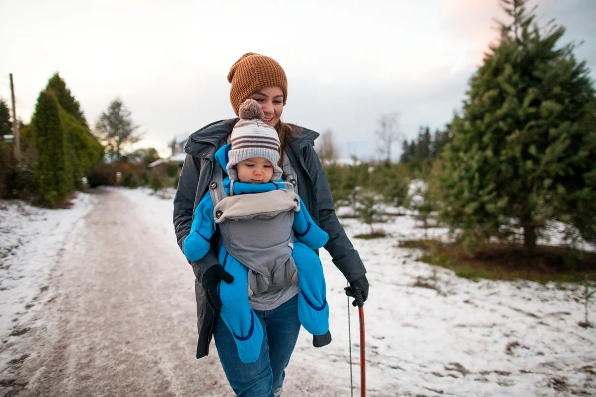 Mother walking with baby in carrier at Christmas tree farm