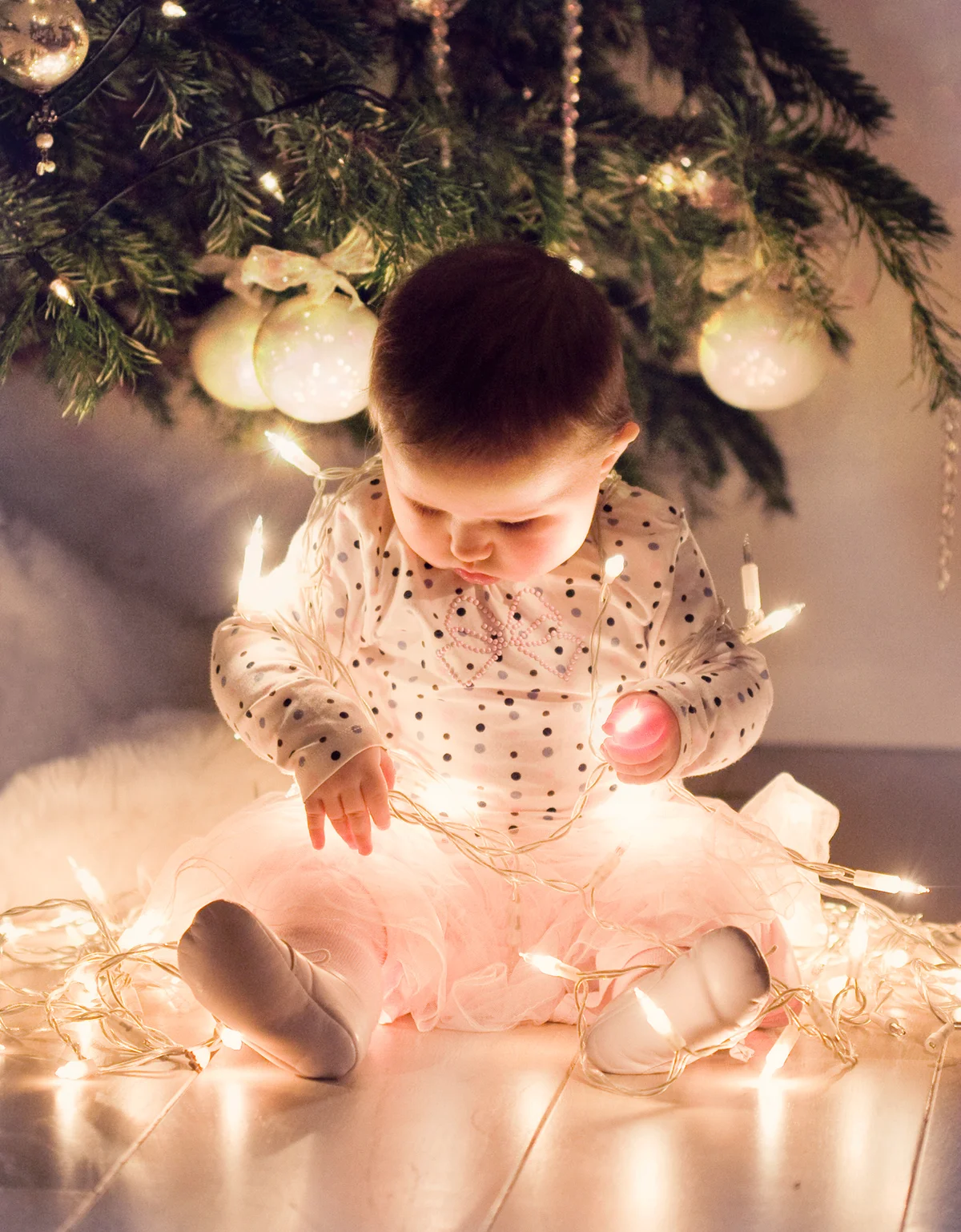 Little girl in tutu skirt is sitting around the Christmas tree