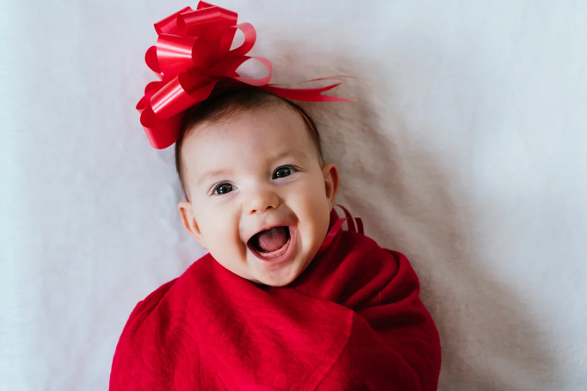 baby girl with red ribbon on her head wrapped in red blanket