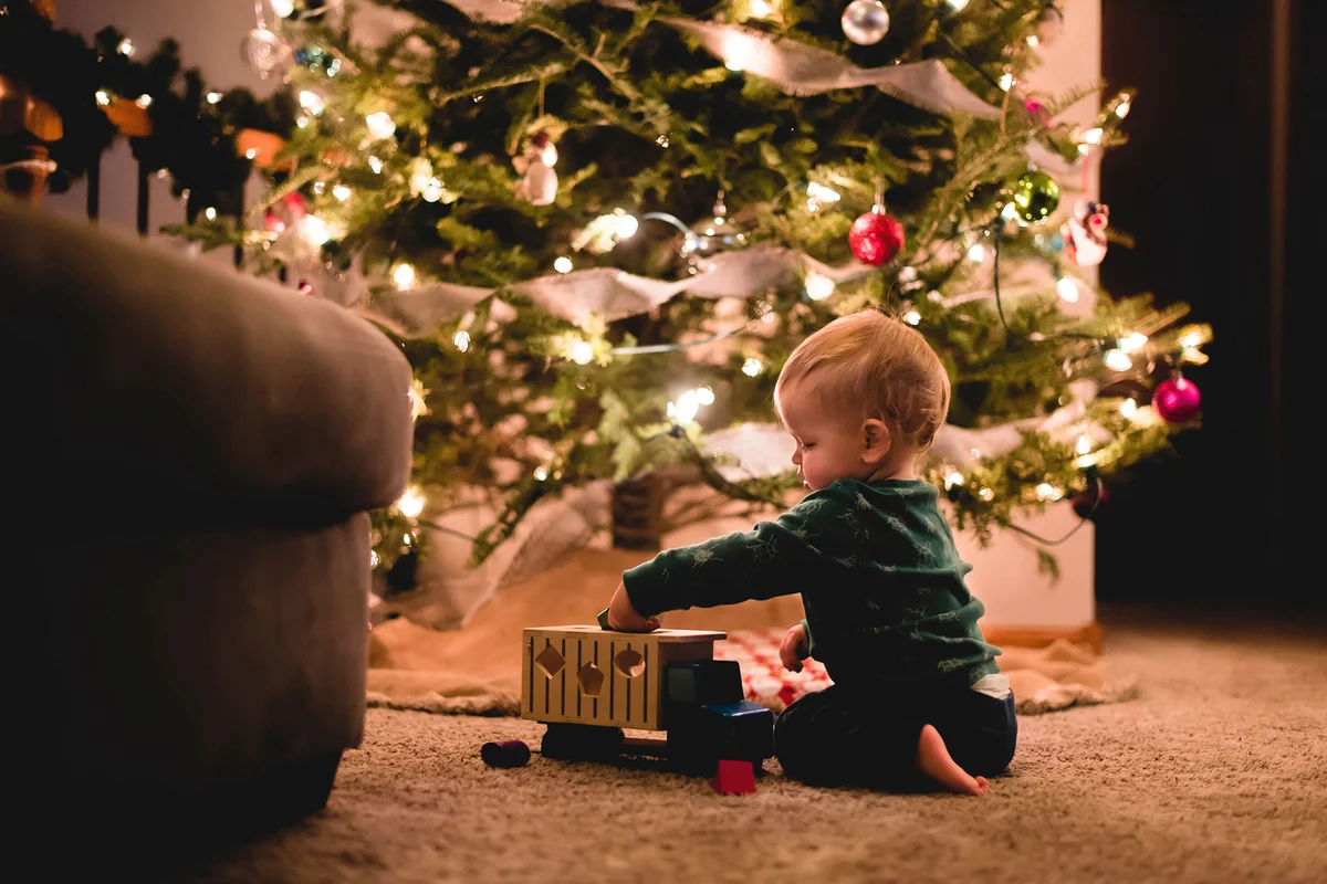 baby boy playing with toy truck by Christmas tree at home