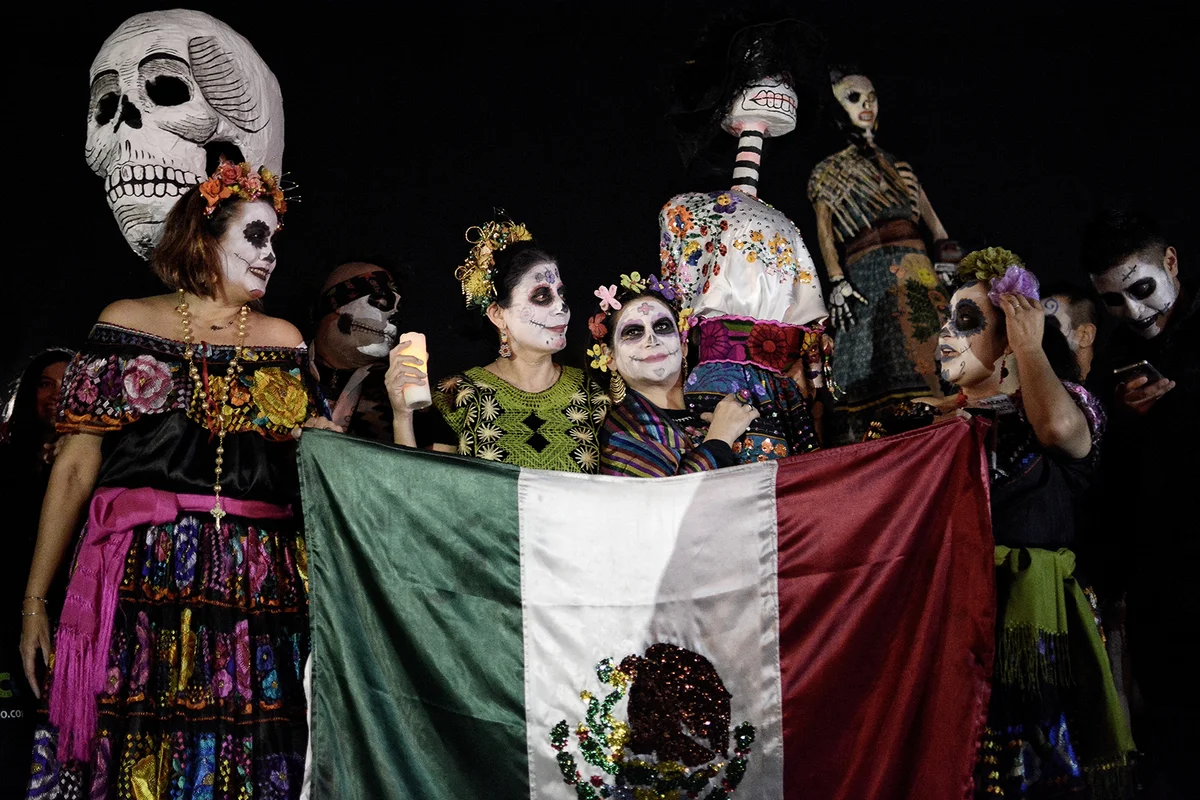 Participants seen dressed as the dead while holding a Mexico flag during the parade