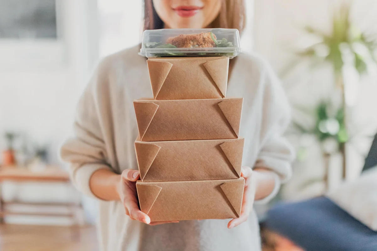 young woman holding a stack of delivery food boxes