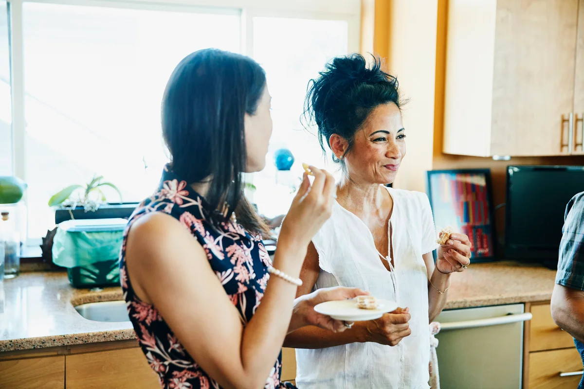Smiling adult sisters hanging out in kitchen eating lunch