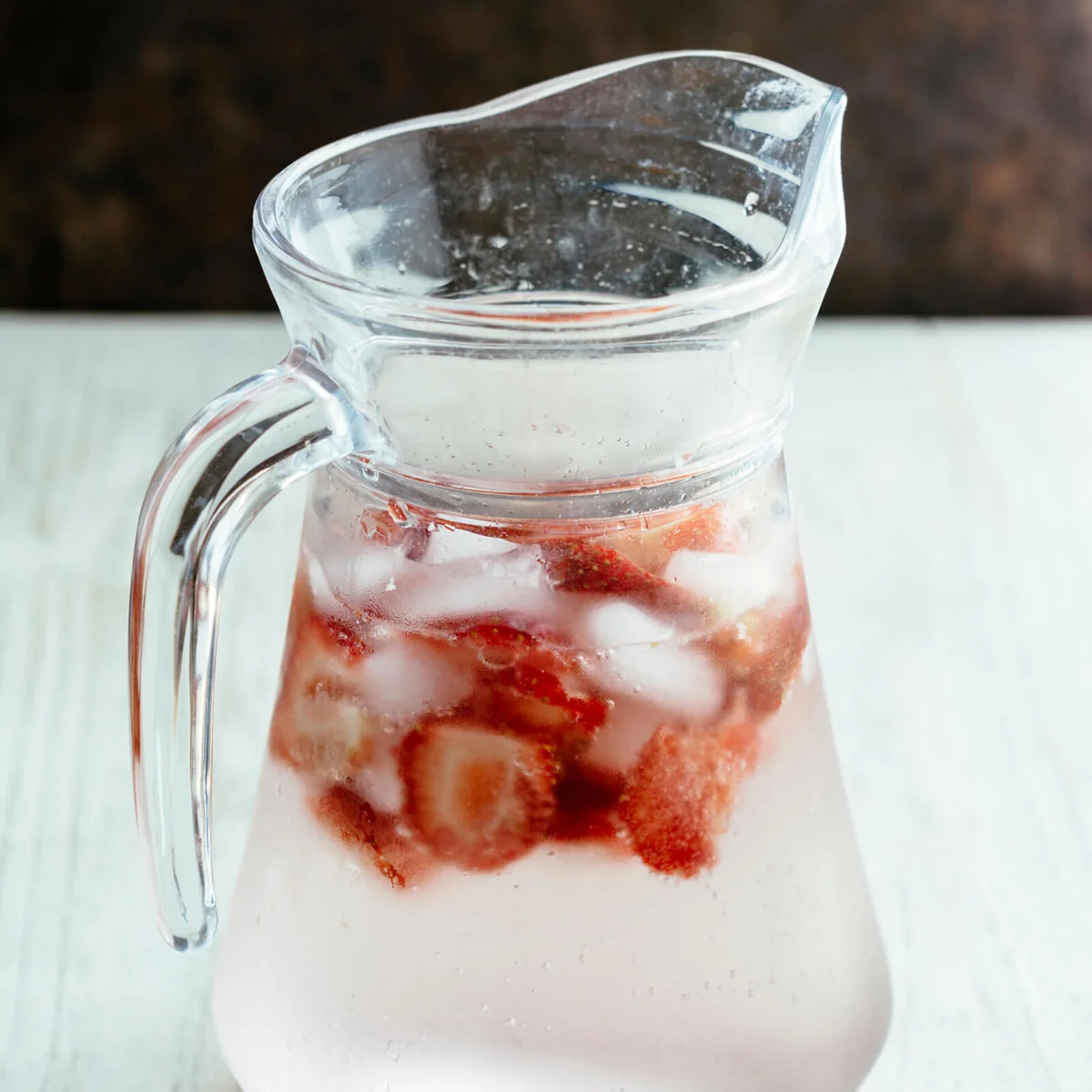 Carafe with sparkling water, ice cubes and slices of strawberries