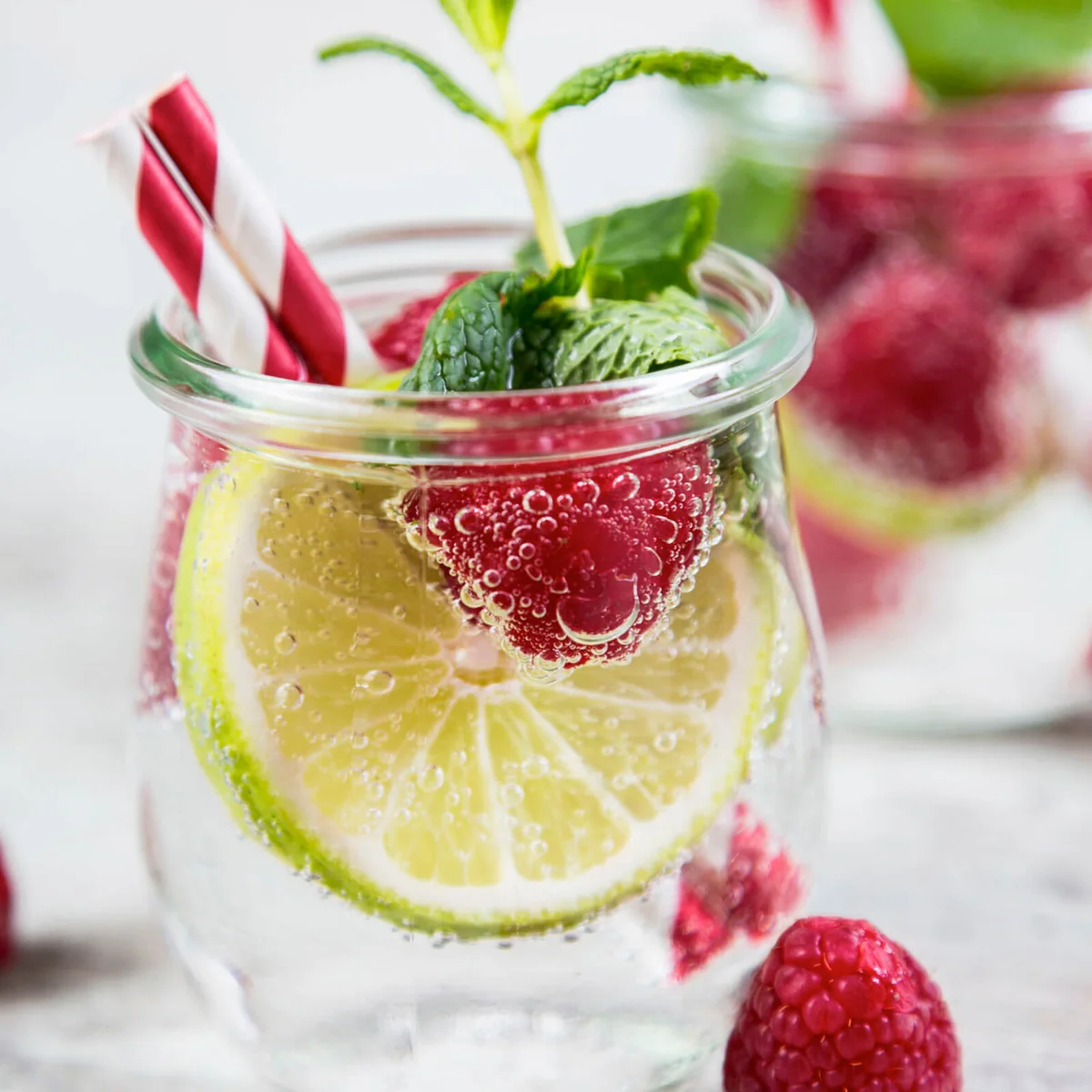Glass of detox water with limes and rasperries decorated with mint leaves
