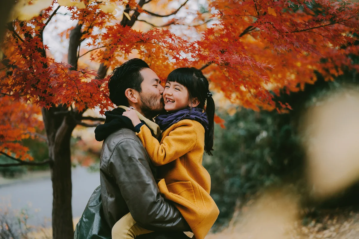 Father kissing cute little girl under autumn leaves