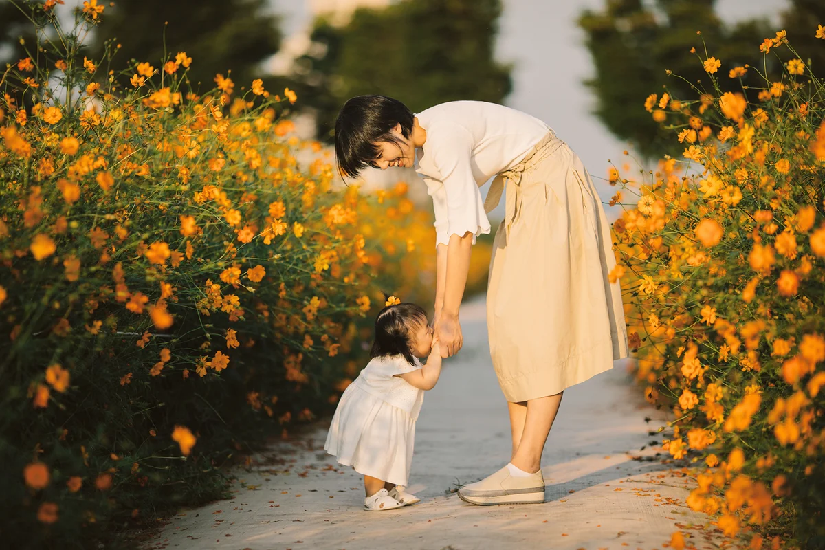 Happy mother with baby in yellow cosmos flower field