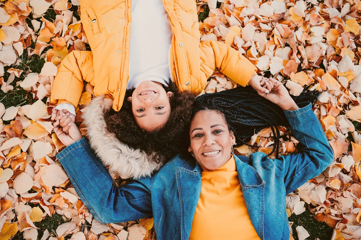 Smiling mother and daughter lying on fallen leaves at park