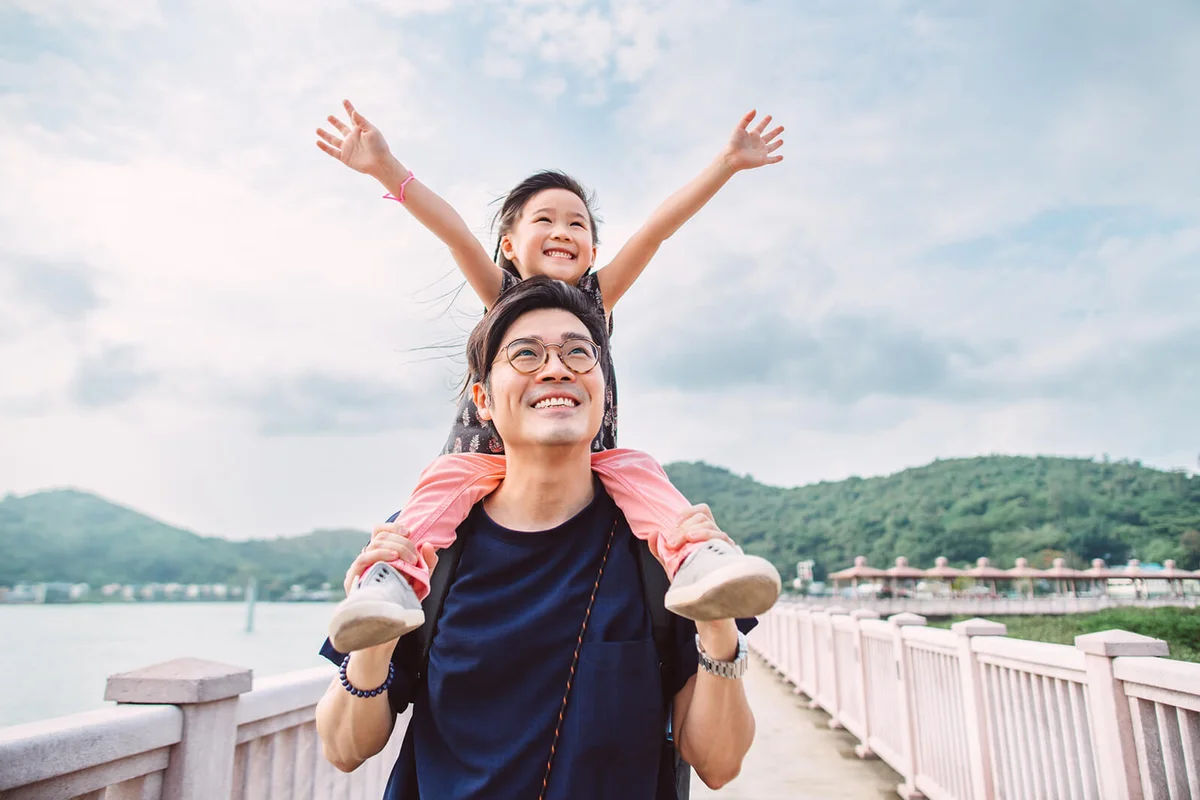 Lovely little girl sitting on dad’s shoulders joyfully