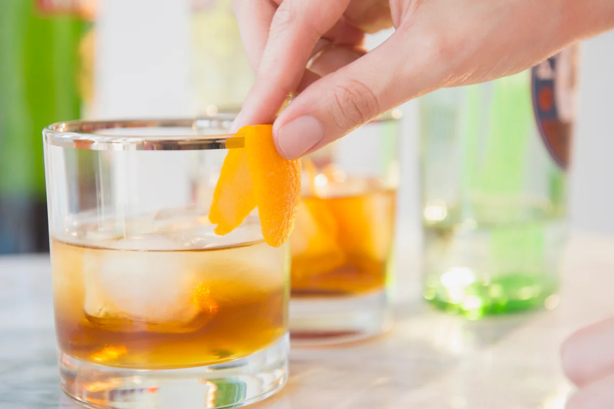Bartenders hand decorating cocktail glass with orange peel