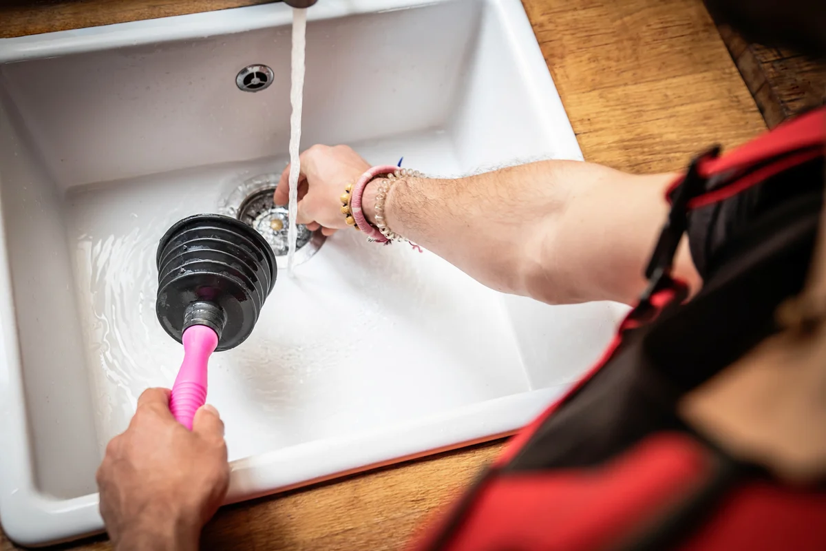 Plumber using a pipe plunger to fix kitchen sink