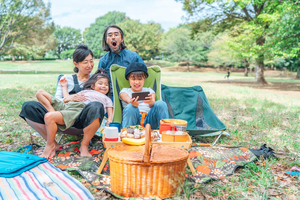 Family having vegan picnic in public park and taking selfie