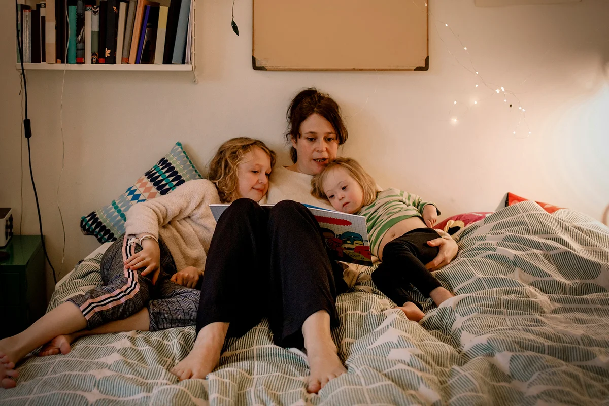mother reading picture book while sitting with children in bedroom