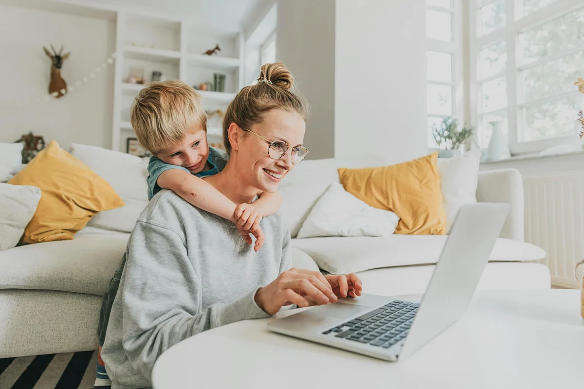 Woman working on laptop while boy hugging her from behind at home