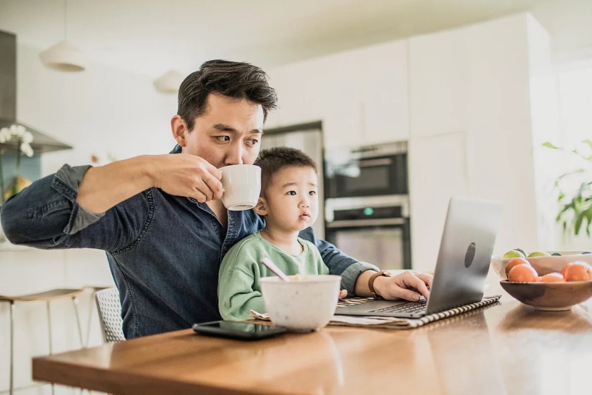 Father multi-tasking with young son (2 yrs) at kitchen table