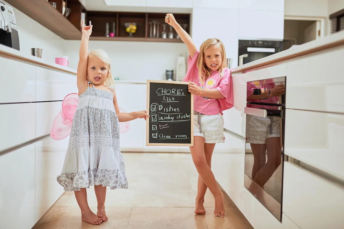two little girl holding a chalkboard with a completed list of chores at home