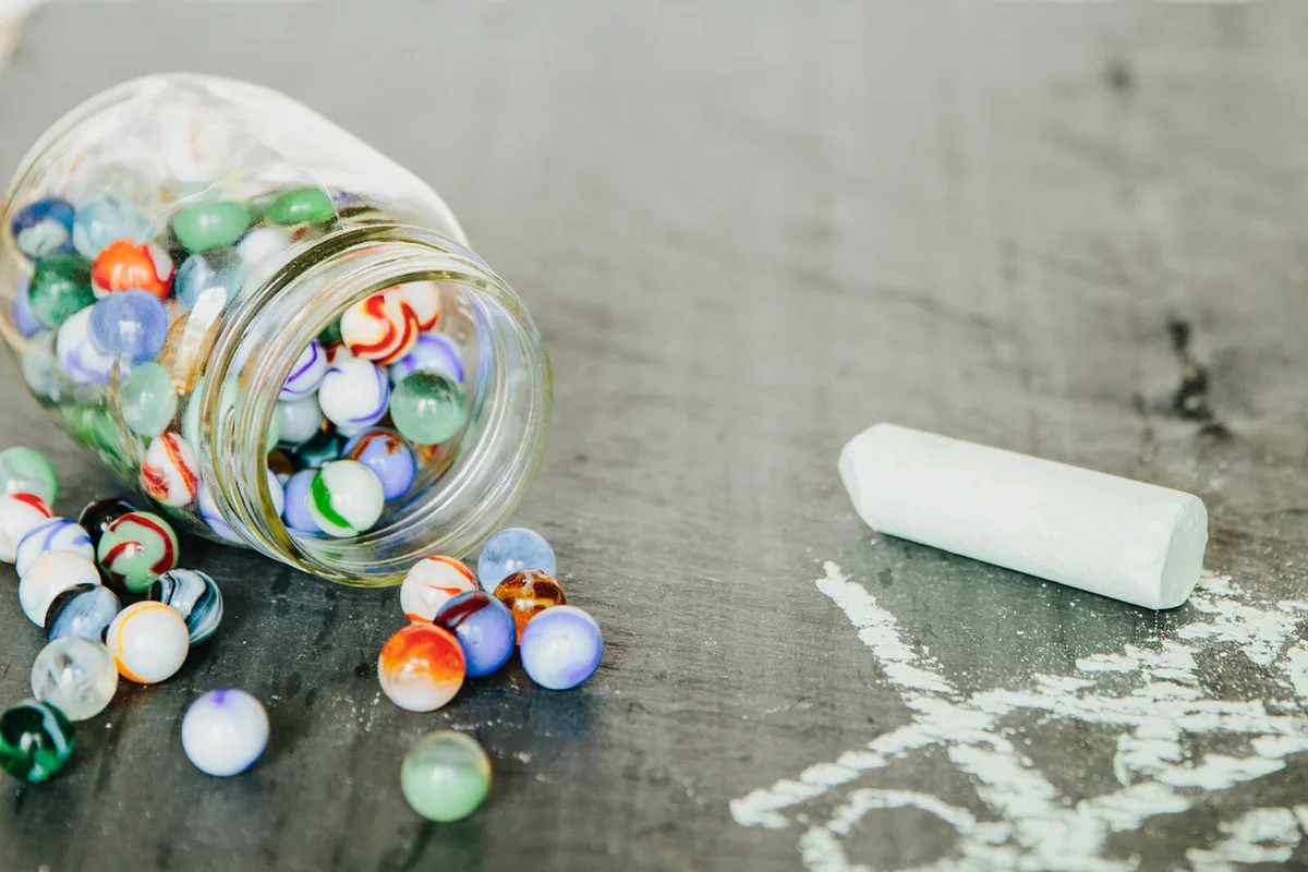 Jar with old marbles and a chalk tic tac toe on black slate
