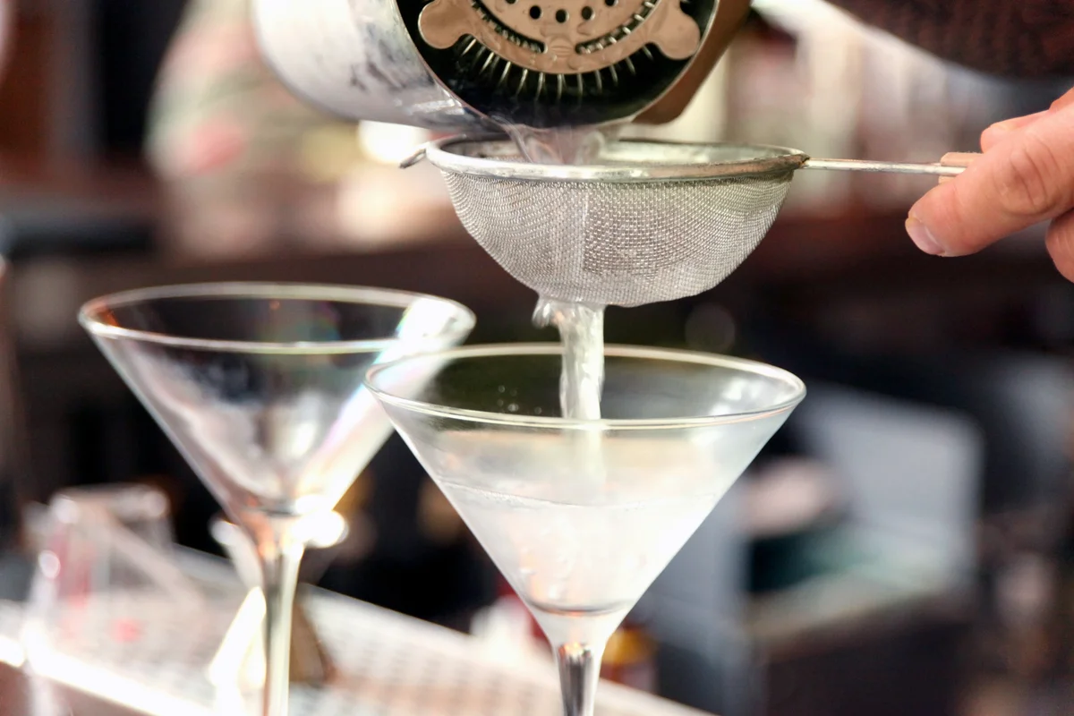 Bartender pouring martinis into chilled glasses