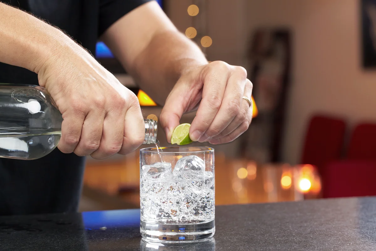 Hands squeezing lime and pouring gin or vodka into lowball glass with seltzer or tonic