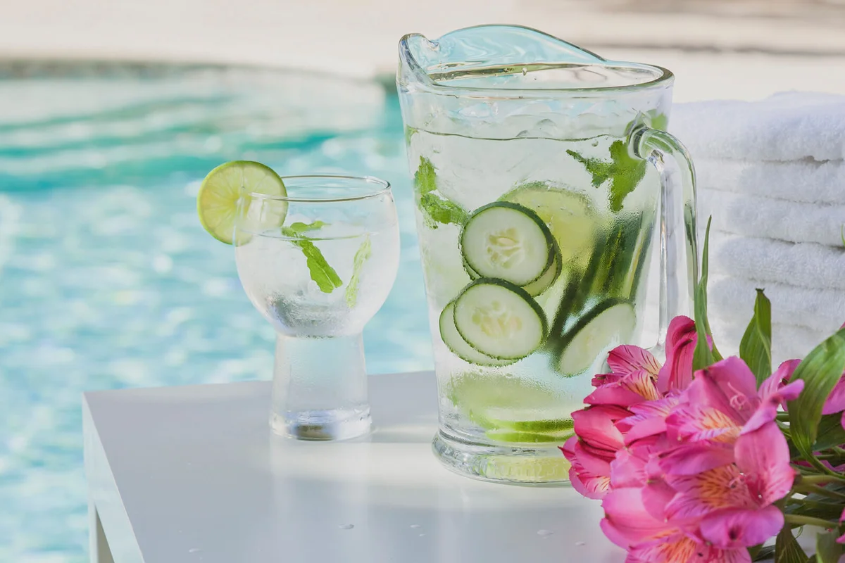 Pitcher and glass of water with cucumber by pool