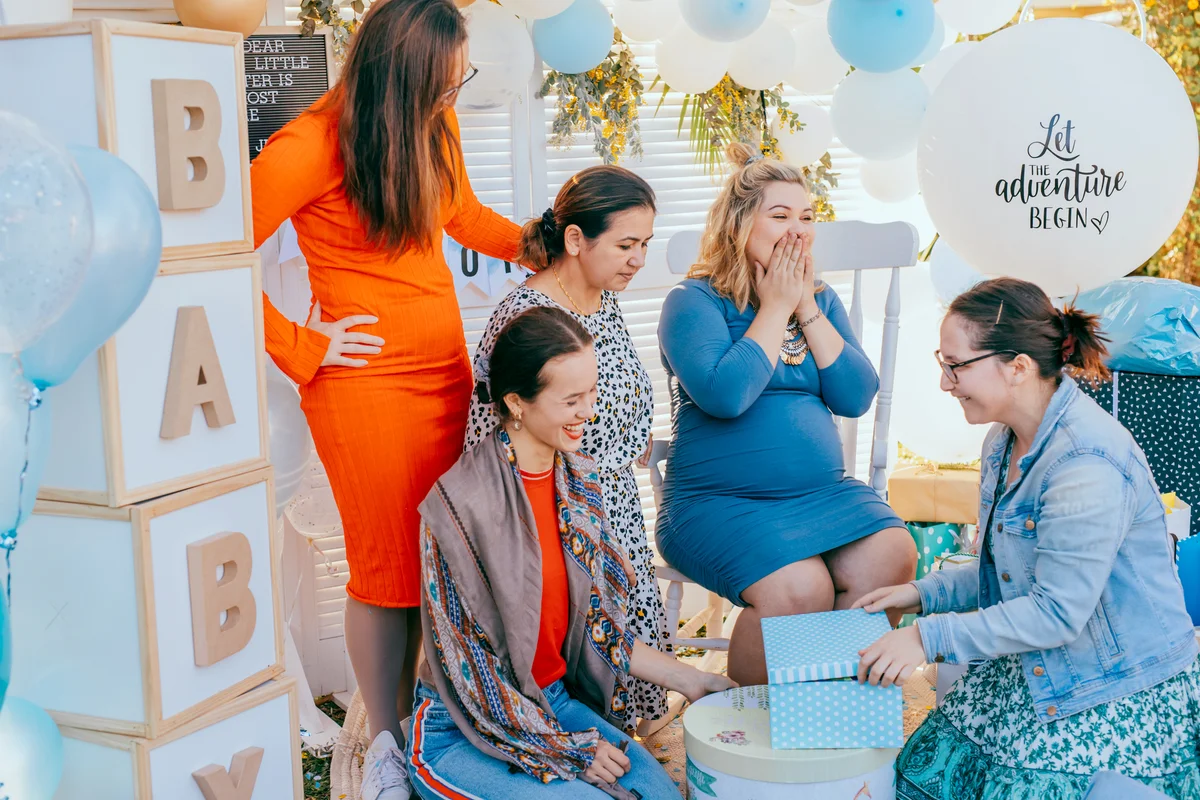 Female friends open gift boxes with a pregnant woman at a baby shower