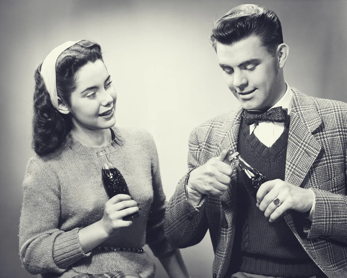 Young couple holding bottles of cola in studio