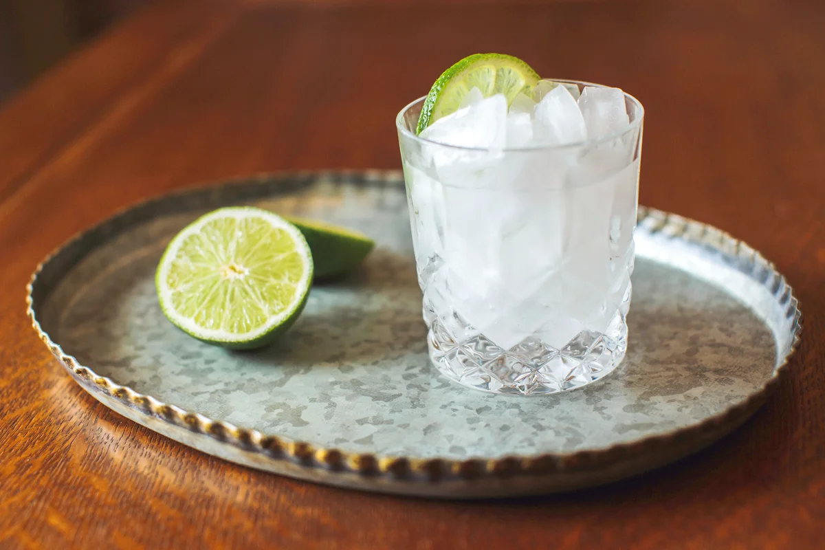 Gin and tonic in a cocktail glass sits on a metal tray