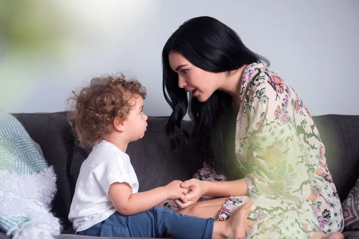 Mother sitting on sofa holding hands and talking with son