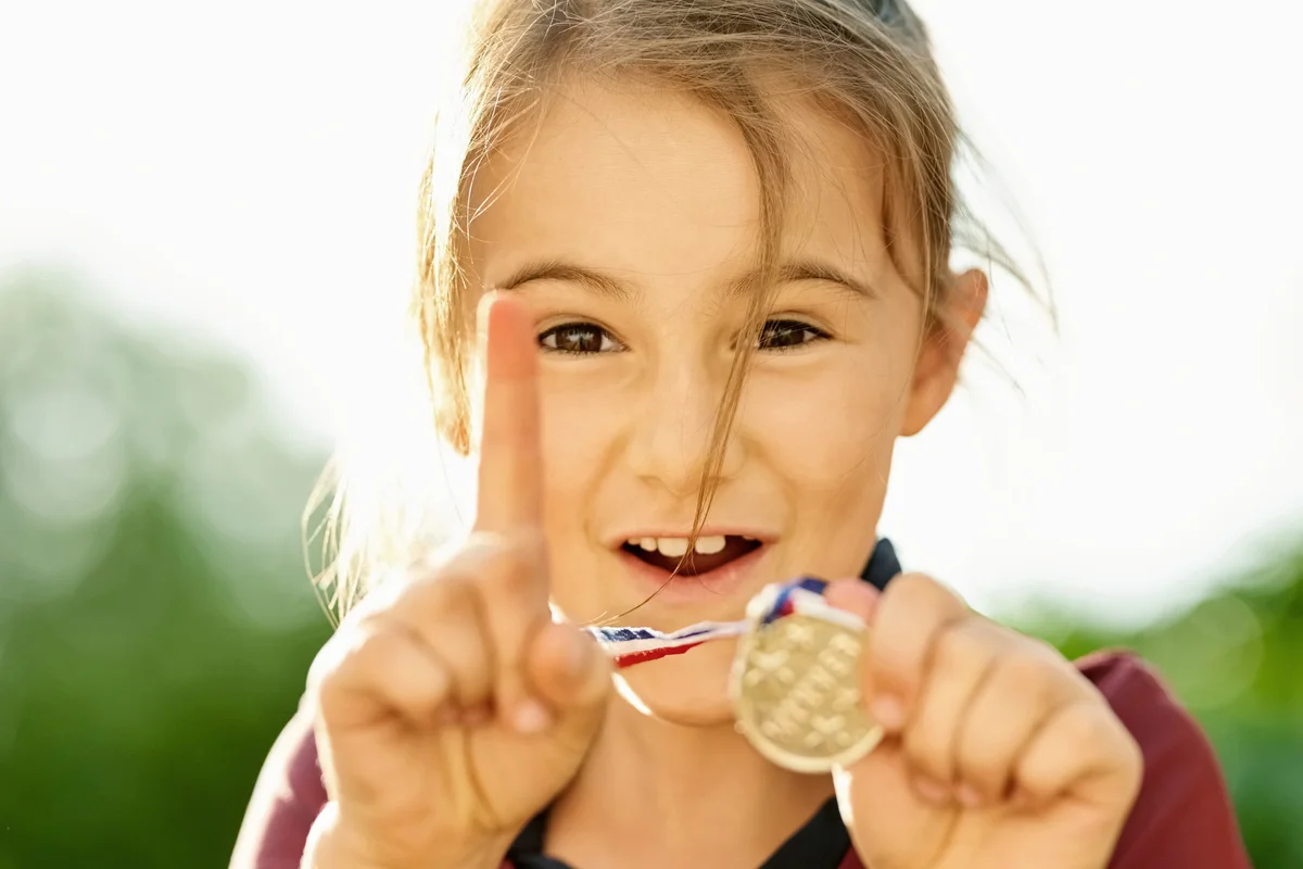 Excited little girl showing her winning medal and gesturing number one