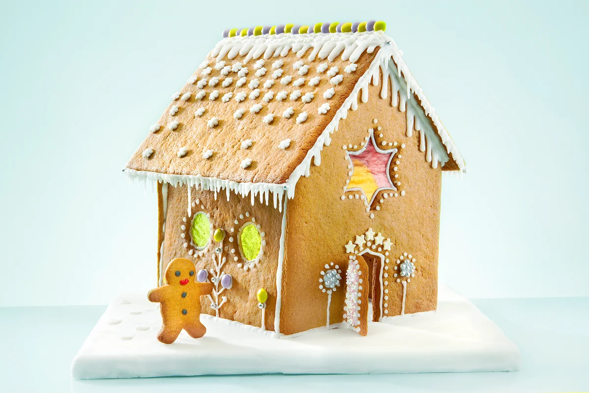 Gingerbread man in front of his colorfull gingerbread house