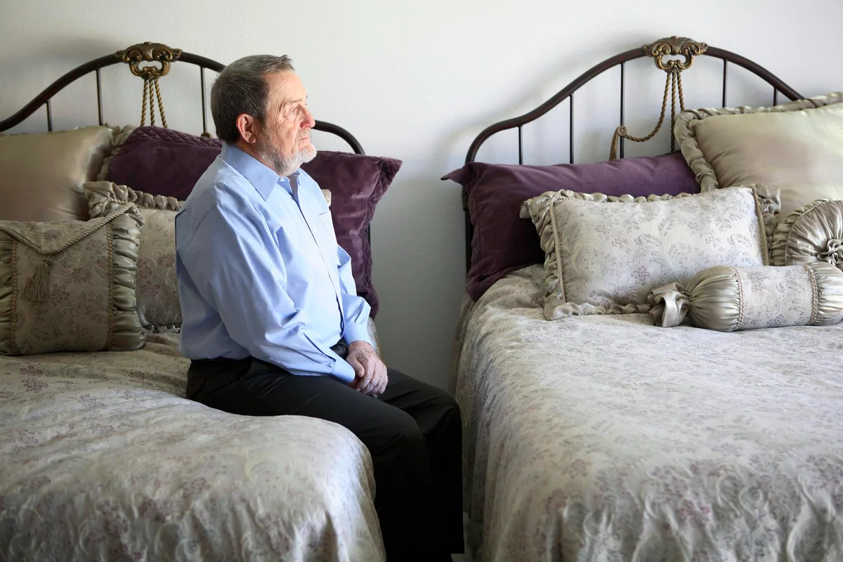 Senior man sitting on edge of his bed and looking to an empty bed in front of him
