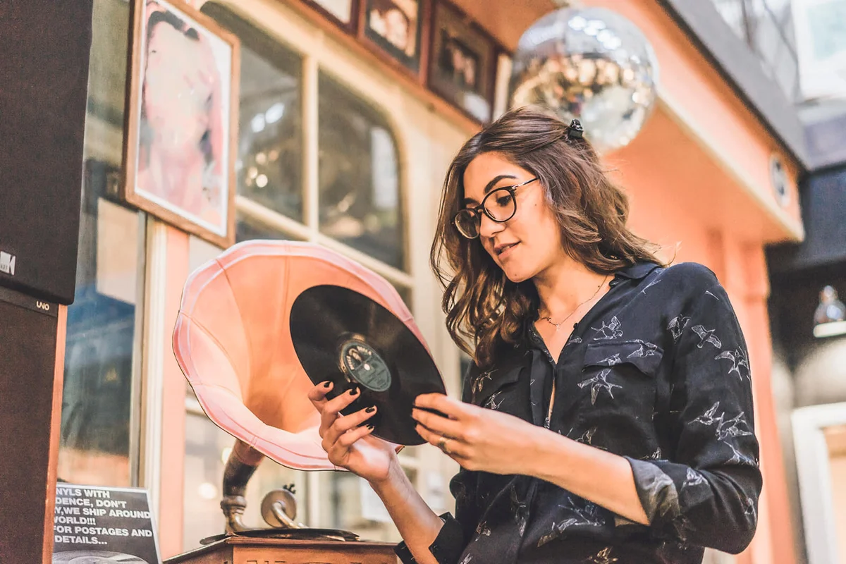 smiling young woman standing in front of antique shop looking at gramophone record