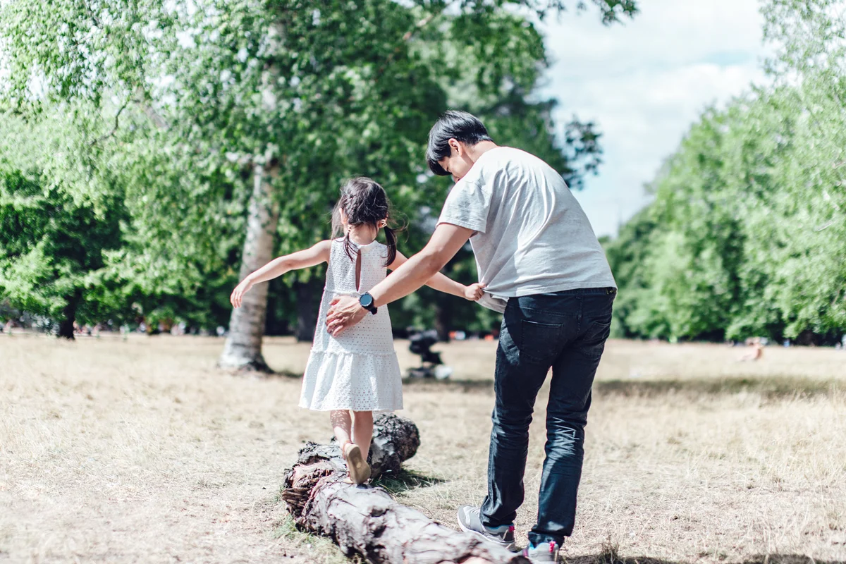 Caring single father assisting his daughter to walk along a tree trunk