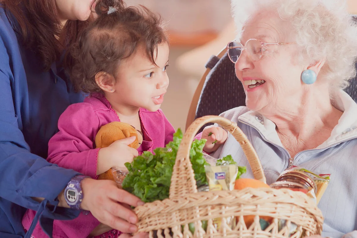 Mother and daughter giving food basket to senior woman
