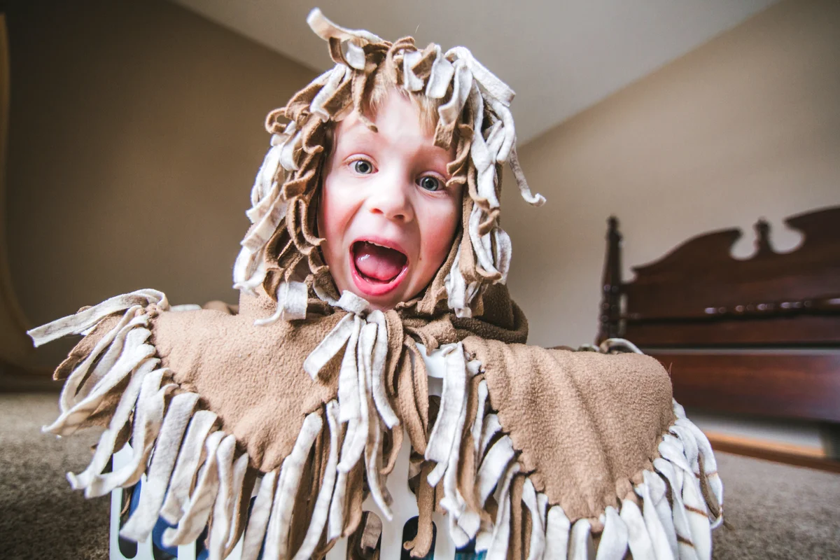 Little boy with a fleece blanket wrapped around his face with fringe from the blanket framing