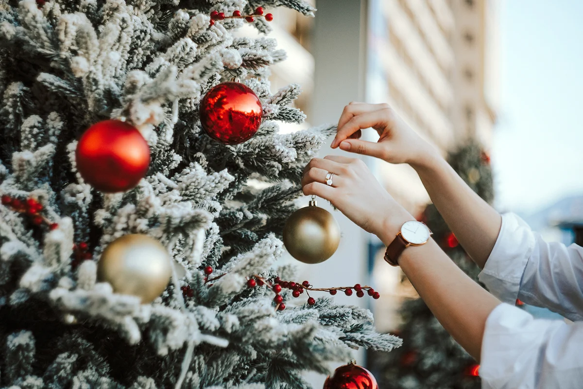 Cropped hand decorating and hanging baubles on Christmas tree