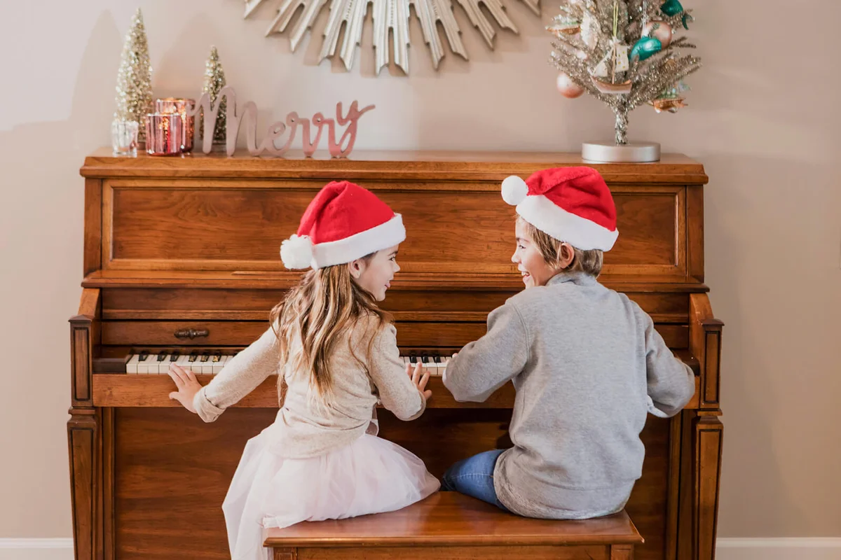 boy and his sister sitting at the piano wearing Santa hats