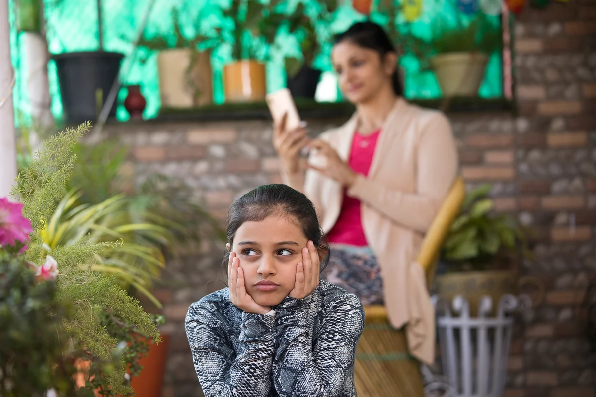 Bored girl with mother using mobile phone