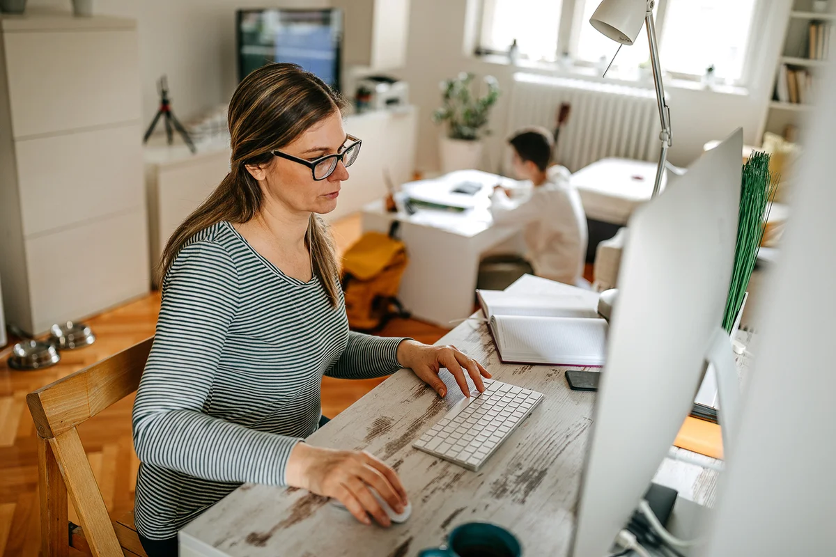 Mother working on computer while son is watching tv at home