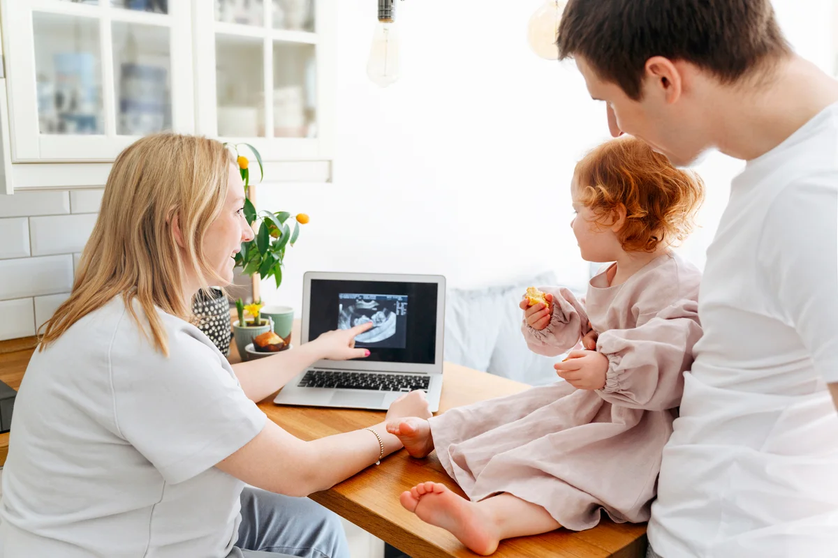 Smiling pregnant woman showing ultrasound image to daughter by father on table in living room