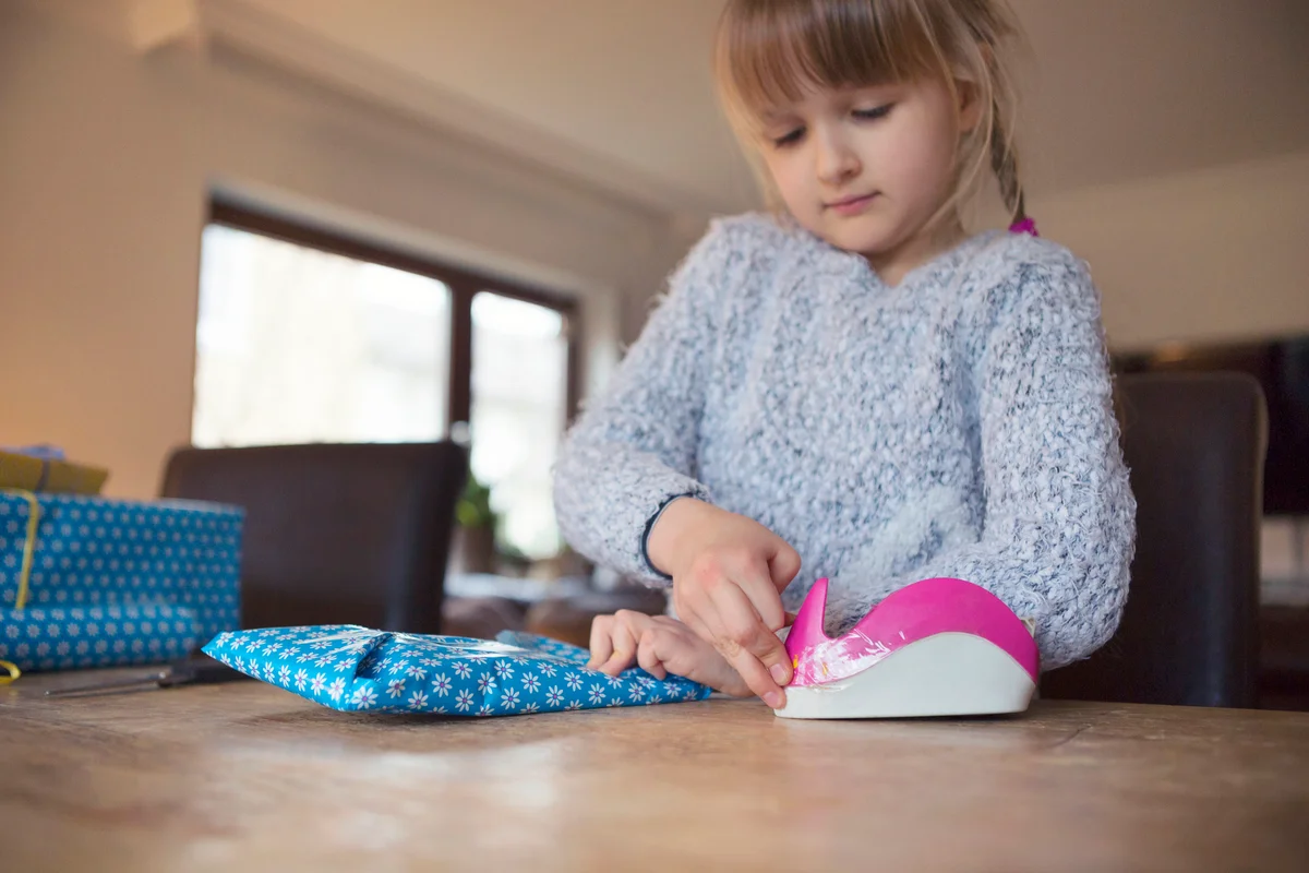 Child using adhesive tape to secure blue wrapping paper around a gift
