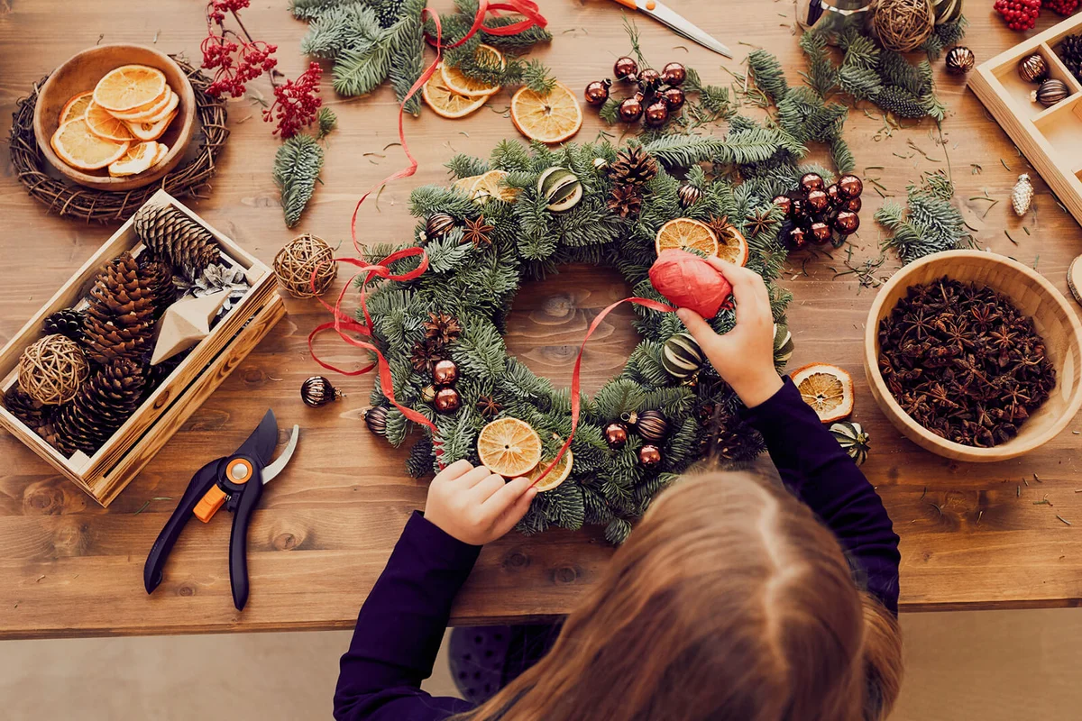 woman standing at desk and using decorative ribbon while making Christmas wreath