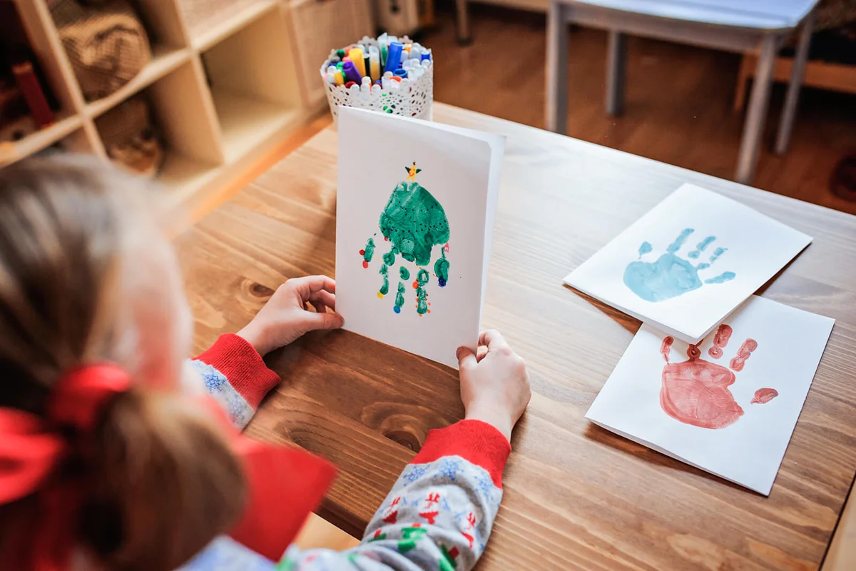 child girl in Christmas sweater making handprints post cards