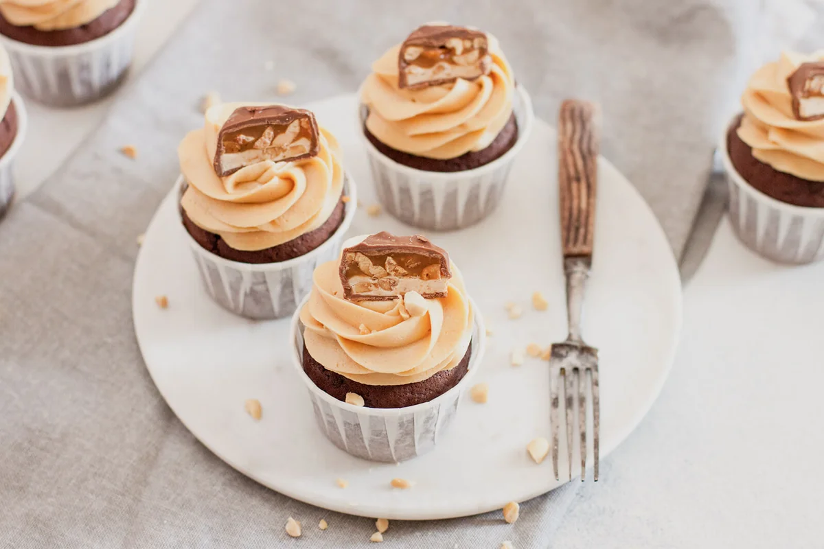 Peanut butter cupcakes with chocolate bites and chopped nuts on grey linen tablecloth