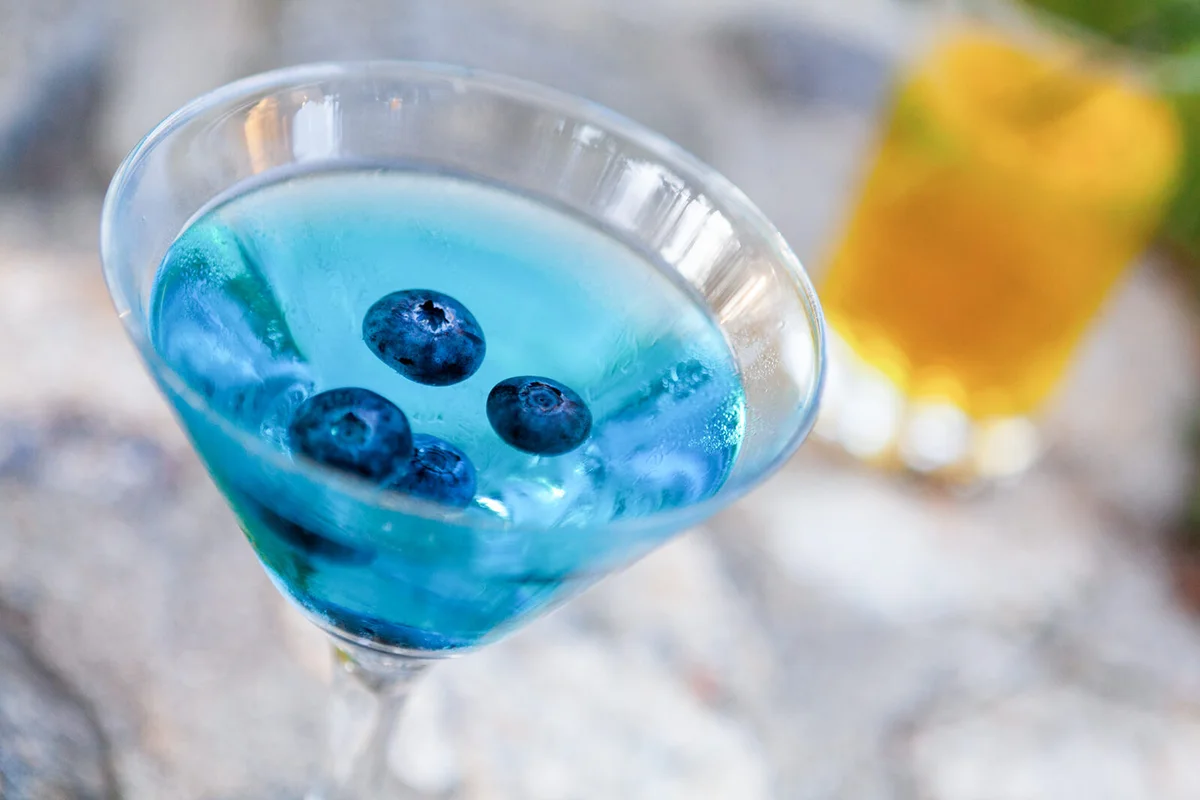 Blueberries floating in blue Martini with second drink in background