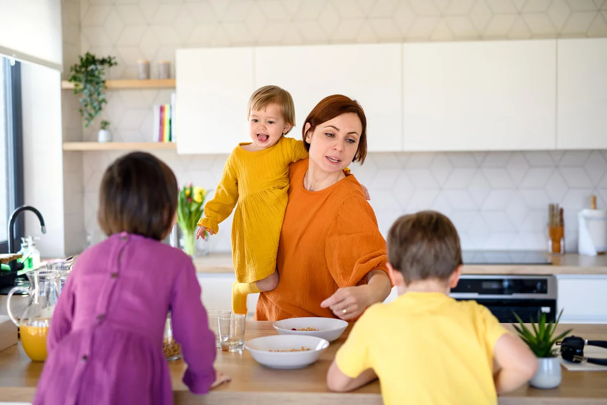 Mother with three small children indoors in kitchen in the morning at home