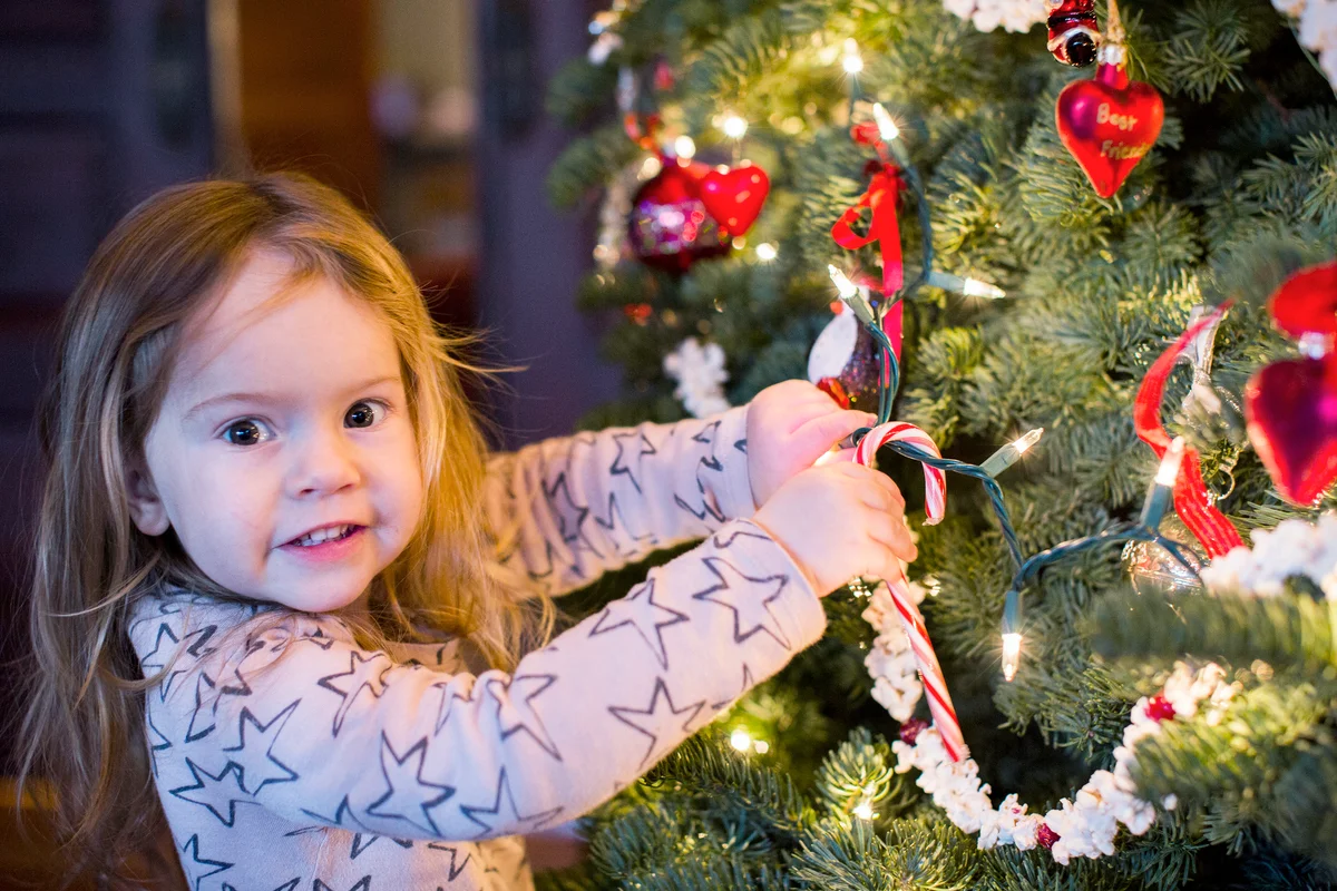 Girl hanging candy cane and popcorn on Christmas tree