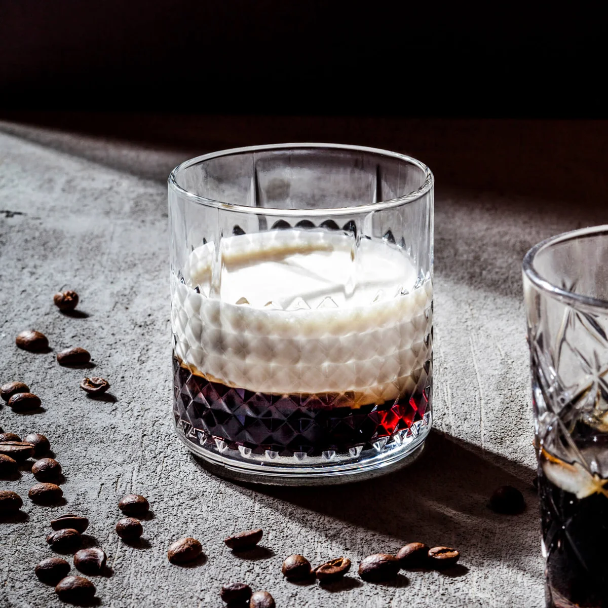 White Russian in glass by roasted coffee beans on concrete table